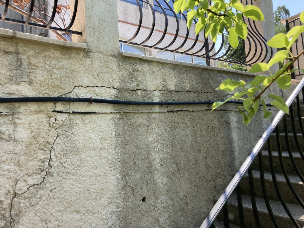 Vertical cracks running through an old rendered retaining wall.