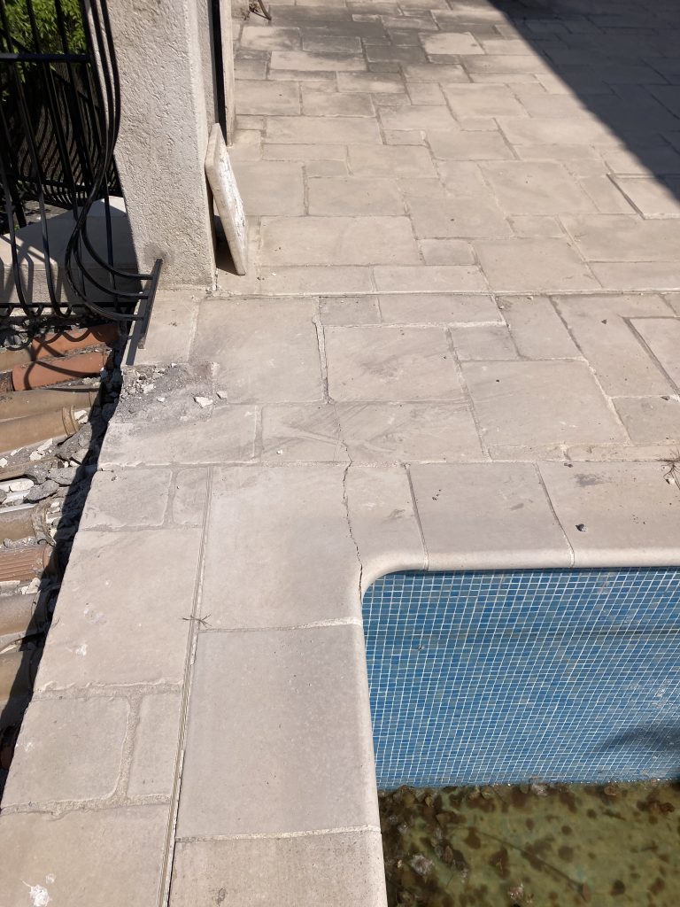 Cracked retaining wall beside metal stair railings.